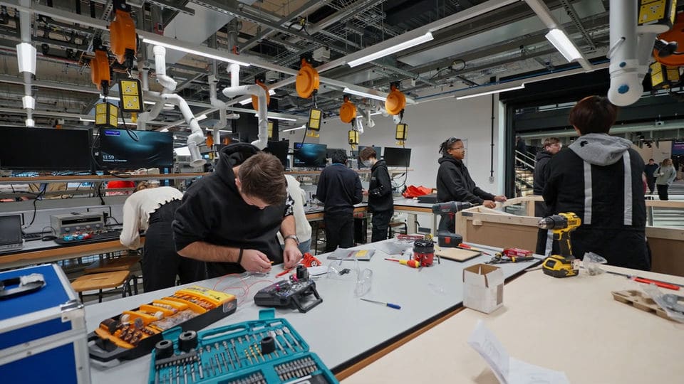 Wide view across the Makerspace workshop with benches, tools, and students working on prototypes.