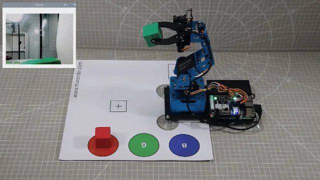 Robot arm sorting colored blocks on a tabletop with color-marked target zones.